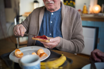 Close-up of senior man enjoying breakfast,spreading on bread in nursing home care center.