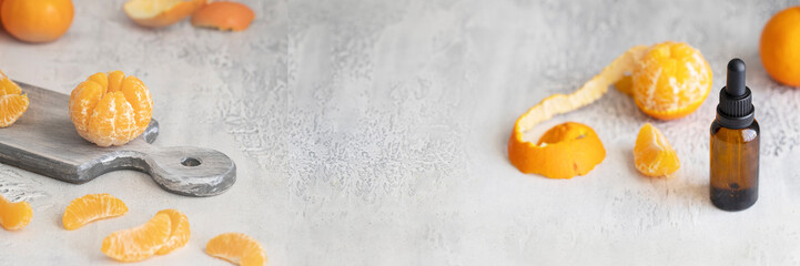 Essential mandarin fruit oil dropper and fresh tangerines slices  fruit on grey background for banner. Aromatherapy and Ayurveda concept.Copy space