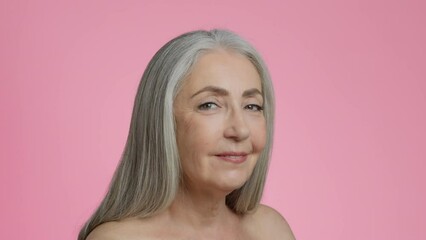 Skin moisturizing. Happy senior grey haired lady applying nourishing serum on cheek and rubbing it, smiling to camera - Powered by Adobe