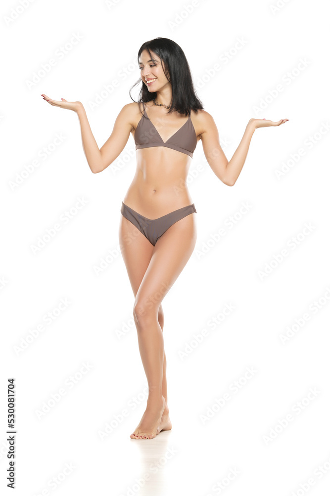 Canvas Prints Young smiling brunette woman in bikini swimsuit advertising imaginary object on her hand on a white background.