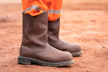 A construction worker is fully wear PPE such as safety shoe and coverall unitform is standing on dirt ground. Industrial worker and equipment object photo. Selective focus.