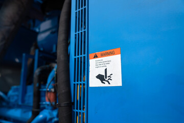 "Machinery rotating part" caution symbol icon on the metal guard of the power generator engine. Industrial equipment and safety sign object photo.