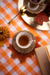 Autumn still life with candles in the shape of pumpkins, tea cup, autumn leaves, teapot, golden spoon and vintage book