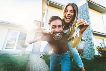Fotobehang Happy young couple holding home keys after buying real estate - Husband and wife standing outside in front of their new house © Davide Angelini