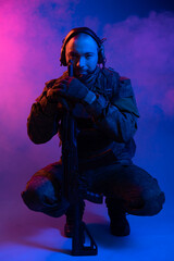 Fototapeta premium soldier in the studio on a blue background. a man in military uniform with a rifle or machine gun in colored light and smoke. military or airball player. blur
