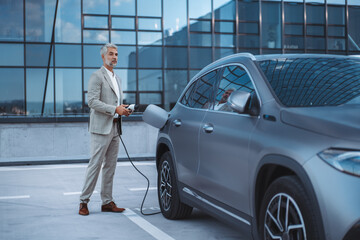 Businessman holding power supply cable at electric vehicle charging station.