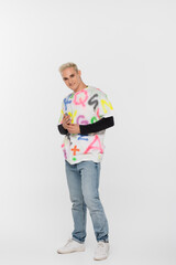 Fototapeta premium full length of blonde fashionable gay man smiling at camera on grey background.