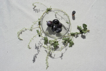 Plums in a transparent cup, surrounded by small white flowers.