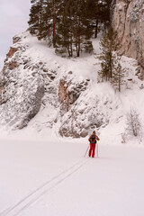 Rear view of young man in red brown clothes with backpack skiing near rocks and cliffs Active healthy lifestyle Winter sports Hiking