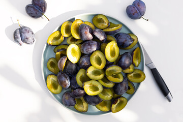Whole and halves of a blue plums lie on a plate. Autumn harvest. Preparatory stage for making jam,...