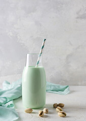 Transparent bottle with pistachio milk on a light table. A light green napkin in the background. Pistachios on the table. Light background