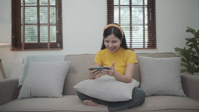 Asian young beautiful woman playing mobile game on smartphone at home.