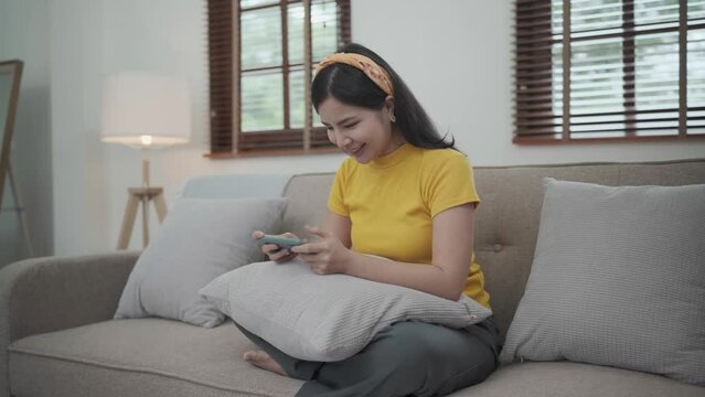 Asian young beautiful woman playing mobile game on smartphone at home.