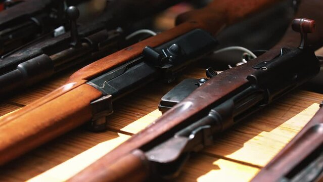 Neat weapons lying down on a wooden table. Various brown-and-black rifles seen from a closeup slow-motion perspective. . High quality 4k footage