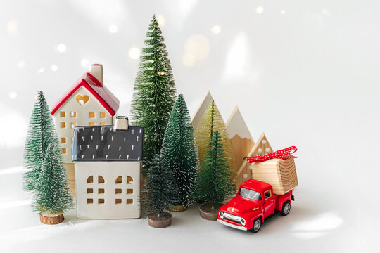 Miniature houses and fir trees with red car with Christmas gift on white background. Winter cute landscape. Cozy small world. Christmas decorations, holiday concept.