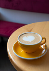 Freshly served cup of cappuccino with latte art on a wooden table in a cafe.