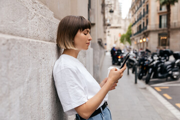 Profile photo of appealing stylish girl with short hair wears white t-shirt and jeans is using smartphone 