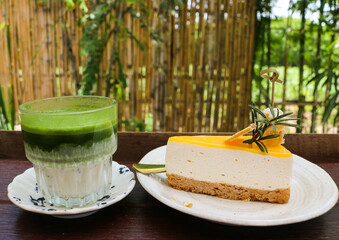 Matcha green tea latte with milk in glass and yuzu cheesecake on wooden table.