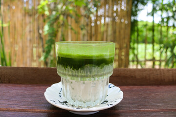 Matcha latte green tea with milk in glass on wooden table.