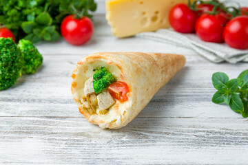 pizza in a cone with chicken, tomato and broccoli on white wooden table