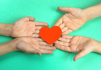 children's hands hold a heart cut out of red paper on a green background. Children give love and warmth concept. Peace love in children's hearts. Children's life and health