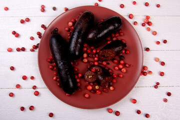 Baked blood sausage on a red plate decorated with red cranberries, Traditional Latvian blood...
