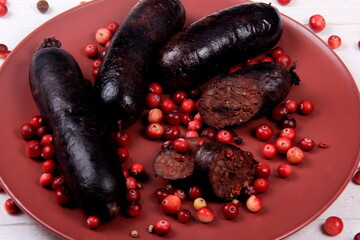 Baked blood sausage on a red plate decorated with red cranberries, Traditional Latvian blood sausages