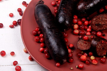 Baked blood sausage on a red plate decorated with red cranberries, Traditional Latvian blood sausages