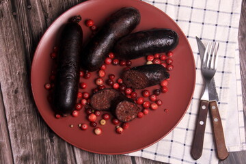 Baked blood sausage on a red plate decorated with red cranberries, Traditional Latvian blood...