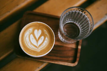 Hot cappuccino in a cup on a wooden tray beside a glass of clear water