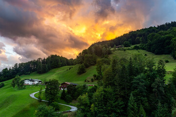 Fototapeta premium Bavarian Mountain Landscape with Meadows, Forest, Cabin and Alps during dramatic Sunset, Germany, Europe