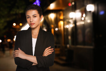 Portrait of hostess in uniform and blurred view of cafe with outdoor terrace at night. Space for...