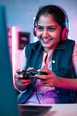 Vertical shot, Smiling girl playing live video game on laptop by talking on headphones at home on neon background - concept of vlogger, gaming addiction and championship © WESTOCK