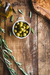 aceitunas variedad manzanilla en un bol, con una rama de olivo y una aceitera de vidrio con aceite de oliva virgen, sobre una mesa de madera rústica, con espacio en blanco