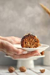 Female hands hold a plate with a piece of cake on a light background
