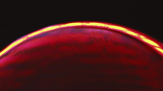 Bubble art. Soap magic. Macro space. Red bulb sphere with bright color fluid zigzags inside contouring yellow line border on black background.