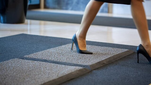 A young business woman wearing high heels enters a modern building wiping her feet on an sanitizing mat. First day of work