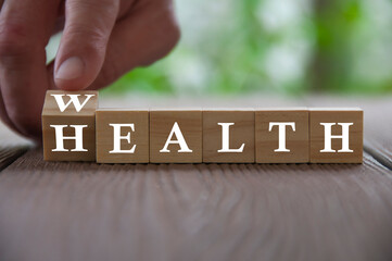 Hand flip wooden cube with word wealth to health with blurred nature background. Wealth and healthcare concept