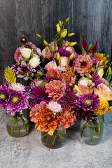 Abundance of garden picked flower bouquets in glass jars. Black background and gray table.