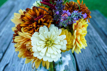 Close up of a bouquet of garden picked flowers in a glass jar. Placed on an outdoor picnic table.  - obrazy, fototapety, plakaty