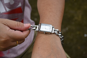 Asian middle aged woman is wearing her wristwatch in her left hand, soft and selective focus.