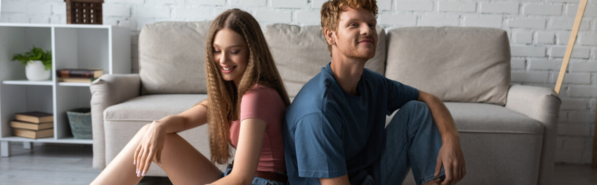 happy young couple sitting next to each other in modern living room, banner.
