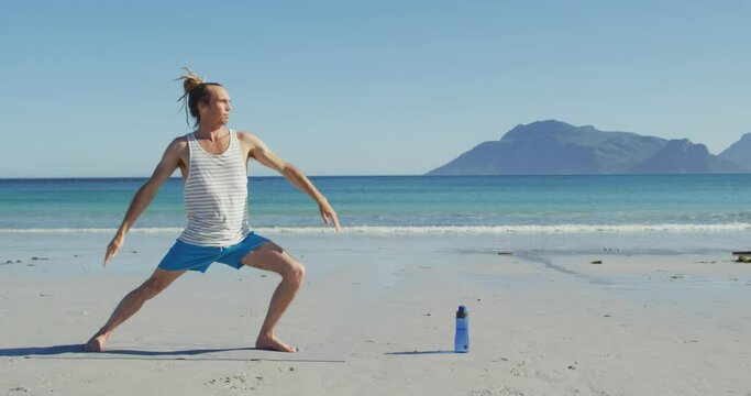Video of caucasian man with dreadlocks practicing yoga standing on sunny beach
