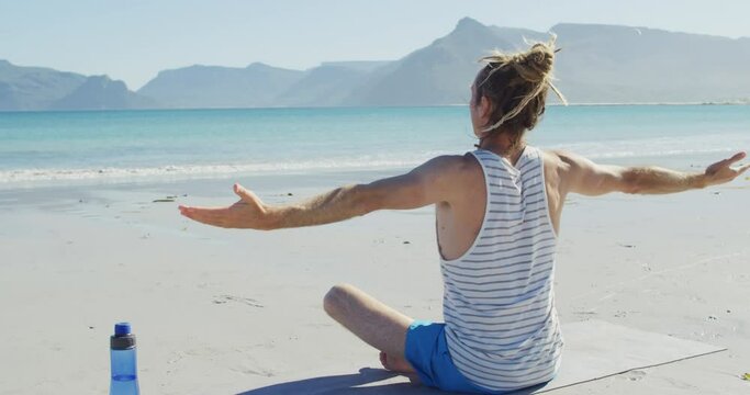 Video of rear view caucasian man with dreadlocks practicing yoga sitting on sunny beach