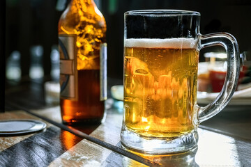 beer mug with beer and a bottle in the bar on the table, light beer. a glass of tasty beer
