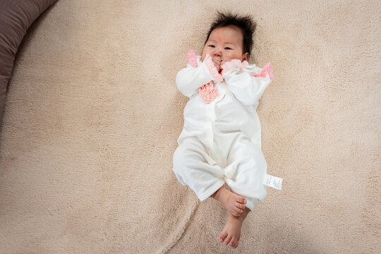 Close-up photo of a 3-month-old Asian baby lying in bed with both hands comfortable to her mouth. And had a happy smile on her face after waking up from her bed as she waited for her mother to come.