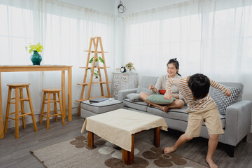 single mother and her Asian son cheer on television on sofa in the living room of the house. The mother-daughter duo express their joy after their beloved team won.