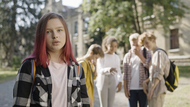 Group of school children bullying sad unpopular girl for distinctive appearance