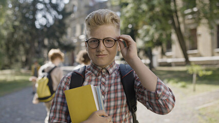 Portrait of smart school boy adjusting eyeglasses and holding books, getting proper education