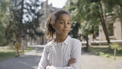 Confident African American school girl posing on camera with arms crossed on chest